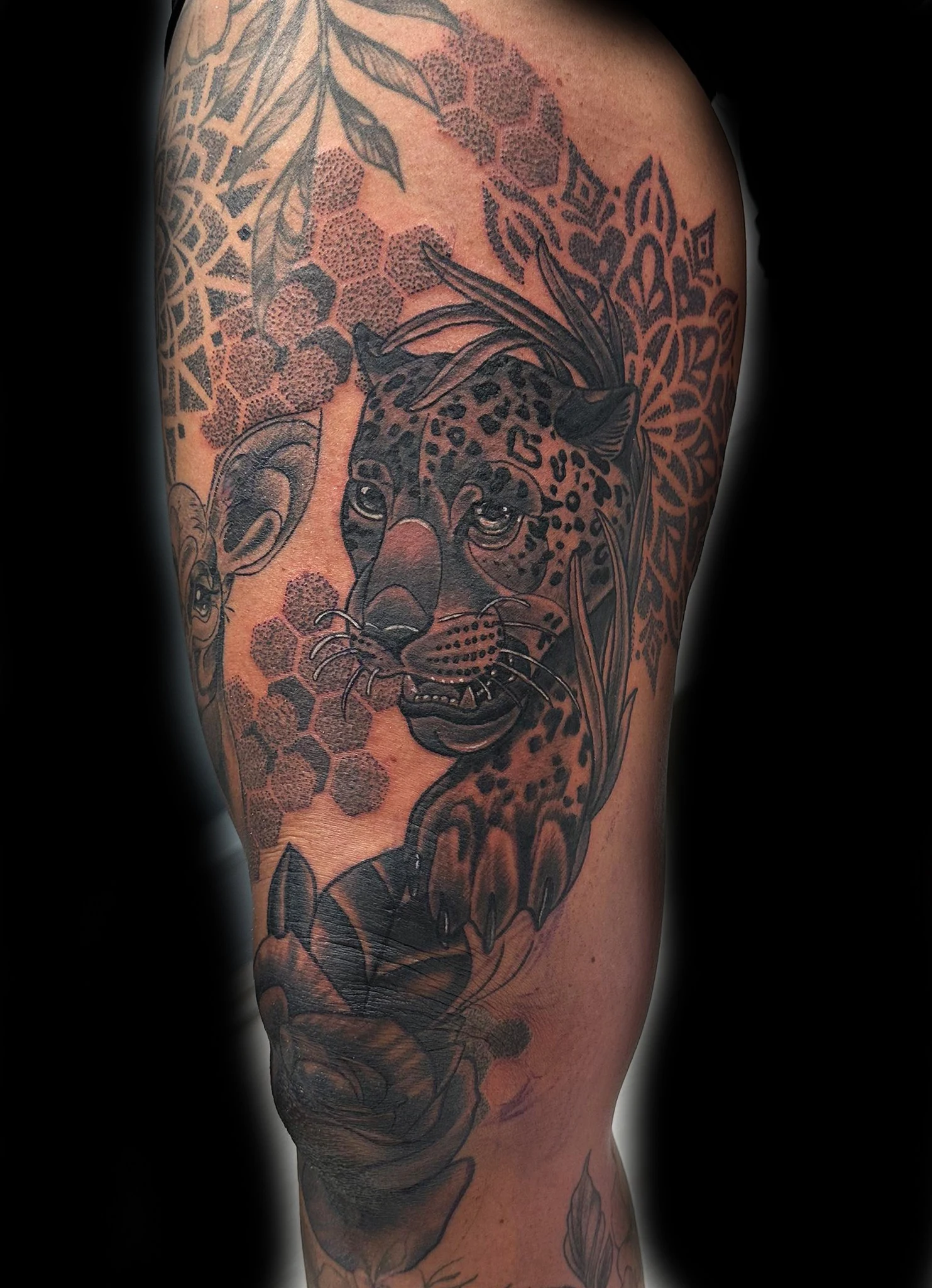 Svart-hvitt tatovering av en leopard med detaljerte prikkmønstre, omgitt av mønster av bikuber og blomstermotiver i bakgrunnen, som gir et harmonisk og detaljert utseende.