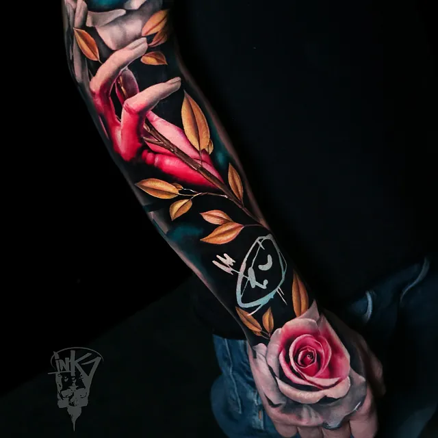 Tatovering på underarmen som viser en rød hånd som griper rundt en gren med gyldne blader og en stor rose i blått og rosa, alle detaljer i et fotorealistisk design.