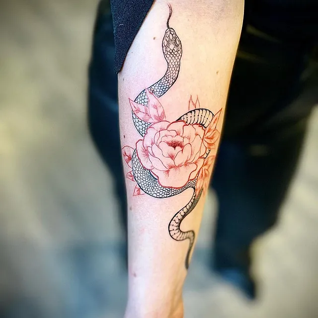 Tatovering av en svartslang som slynger seg rundt en stor, detaljert blomst med delikate kronblader.