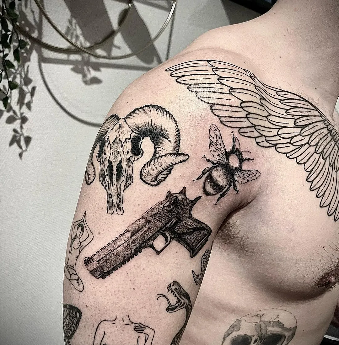 Tatovering på skulderen med en samling av motiver, inkludert et geitehodeskalle, en bie, en pistol, og en engleving, alle utført i svart blekk.