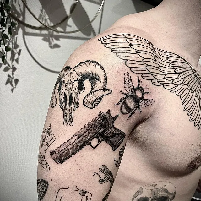 Tatovering på skulderen med en samling av motiver, inkludert et geitehodeskalle, en bie, en pistol, og en engleving, alle utført i svart blekk.