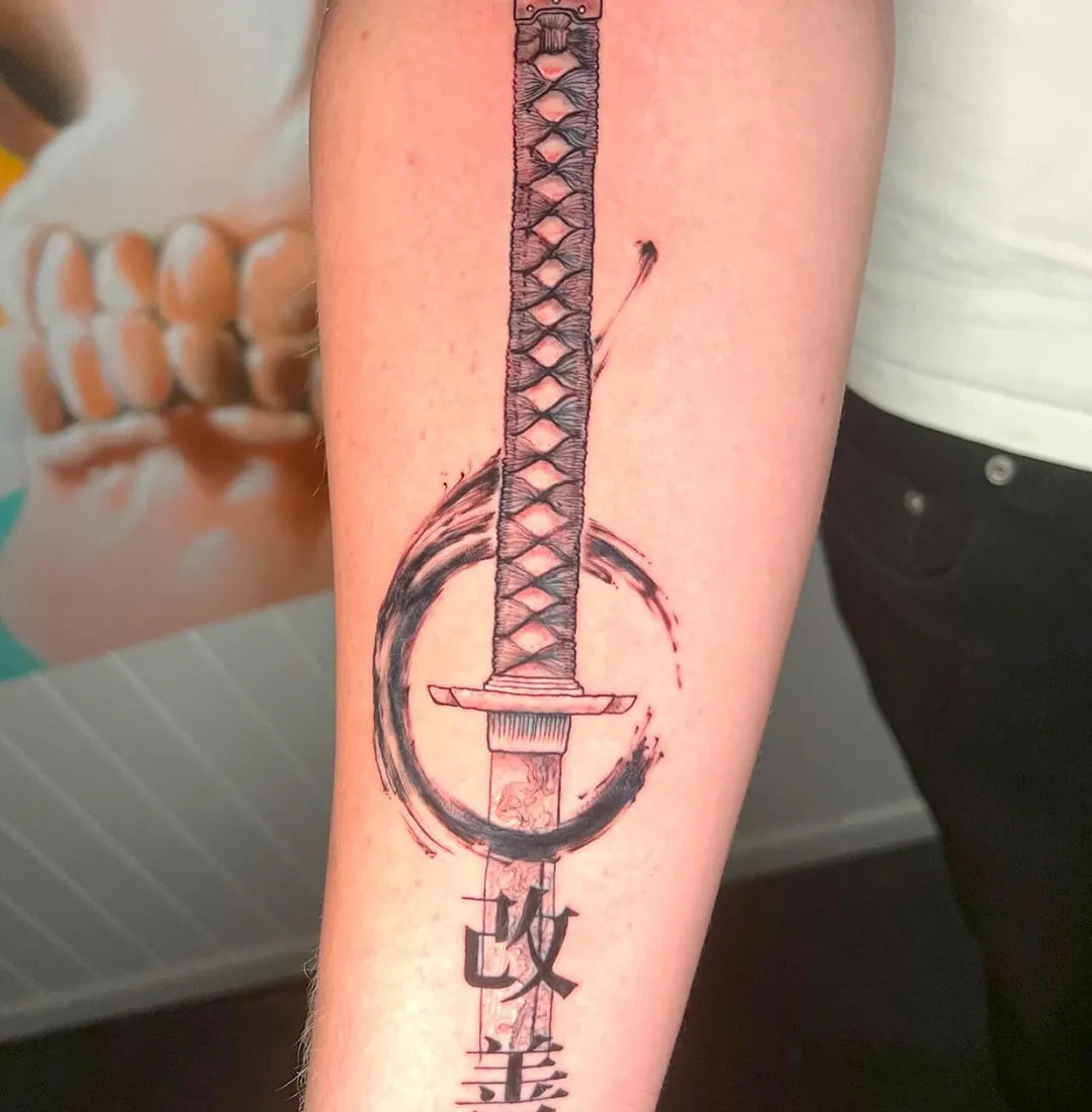 Tatovering av et tradisjonelt japansk sverd (katana) omgitt av en svart sirkel, med japanske tegn nederst på bladet.