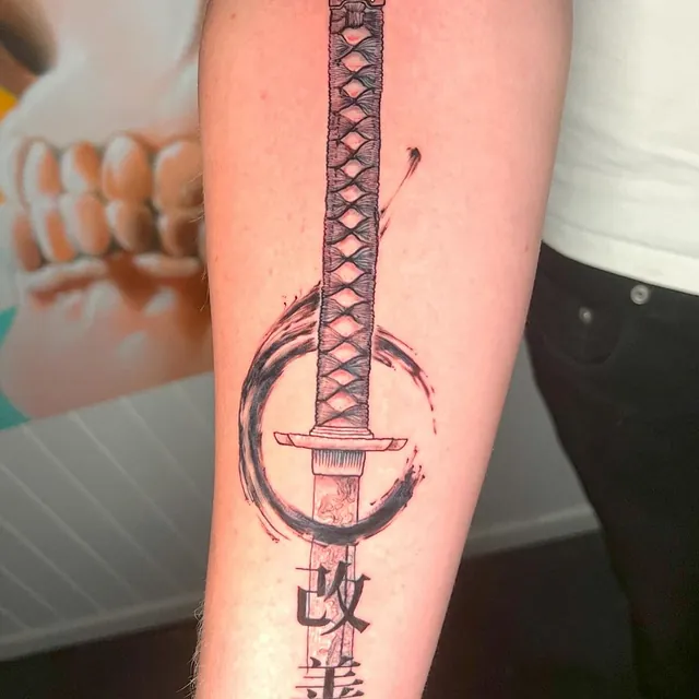 Tatovering av et tradisjonelt japansk sverd (katana) omgitt av en svart sirkel, med japanske tegn nederst på bladet.